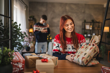 young woman wrap Christmas gift with festive decorations at home