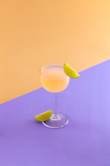 Pink cocktail standing on purple surface with lime garnish