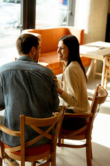 Couple enjoying refreshing drinks and laughter in a cozy cafe on a sunny afternoon
