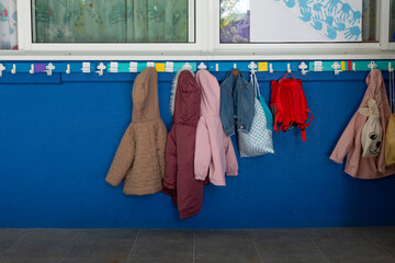 Clothes hanger in a children's school. Children's jackets and backpacks. blue wall © casavella
