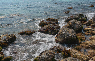 Small waves breaking on the coastal rocks form foam sparkling in the sun