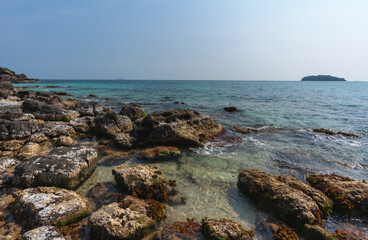 The rocky shore of a tropical island with blue water and a distant island on the horizon