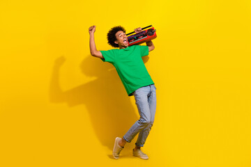 Full length photo of lucky funny guy wear green t-shirt dancing singign enjoy boom box songs emtpy space isolated yellow color background