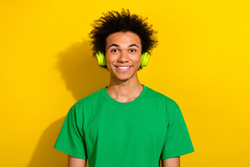 Photo of cheerful positive guy dressed green t-shirt headphones enjoy music emtpy space isolated yellow color background