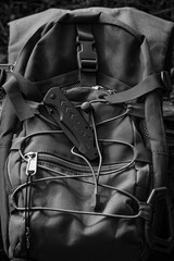 Versatile camping equipment: a brown backpack and a folded pocket knife. Black and white vertical close-up photo.