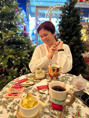 Millennial woman enjoys festive Christmas meal at decorated table, surrounded by Christmas trees and twinkling lights, capturing warmth and joy of holiday season. Joyful expression and cozy setting