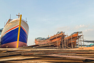 Fototapeta premium Pile of wood or slabs of shipbuilding materials with ships in the background at the Slamaran Pekalongan shipyard in the afternoon
