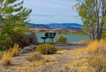 Quiet peaceful setting with empty bench near water part reservoir in cody, Wyoming. Chugwater red butte mountain is in distance.