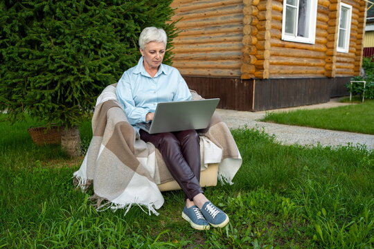 Mature woman working on laptop outdoors near log cabin
