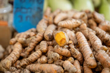 A pile of turmeric roots heaped on a stall for sale. One of them is cut open.