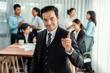 Portrait of happy businessman looking at camera, making finger pointing gesture for advertising product with motion blur background of business people movement in dynamic business meeting. Habiliment