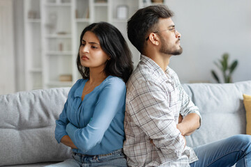 Indian couple sitting back to back on couch at home, upset spouses offended after quarrel,...