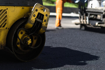 Workers use a roller to compact asphalt on a road construction site in the afternoon sunlight, showcasing construction efforts
