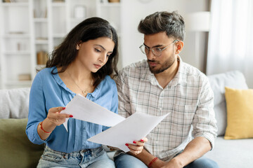 Indian couple checking bills, reading documents, unhappy man and woman holding papers