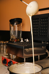 Food preparation. Making Belgian waffles. Female hand pours dough into waffle maker in kitchen at home. Breakfast. Liquid dough poured waffle iron machine to prepare Belgian waffle. Cooking process.