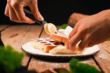 Adding banana on waffle. Topped powdered sugar. Homemade simple pastries. Belgian waffles on wooden table. Belgian waffles on a white plate. Waffles on plate. Ice-cream topping. Cooking process.