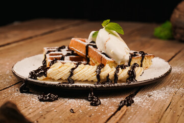 Sweet dessert waffles. Served with ice cream. Belgian waffles with banana, ice cream and chocolate on top. Delicious dessert for tea time. Mint on top of dessert. Cooking process.