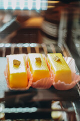 A view of a display of assorted European pastries,inside a bakery shop. Yellow beautiful cheese desert laying down on a black plate for sell, front view.