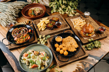 Top view of gourmet food dishes including sausages, ribs, schnitzel, salad, and burger on table