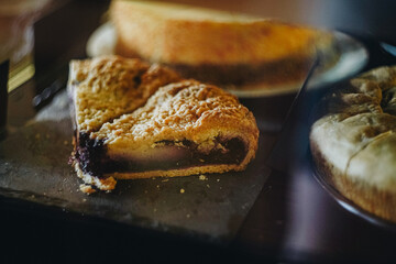 Two pieces of blueberry pie and cheesecake on background on black plate in display case at cafes....