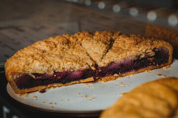 Delicious variety of cakes and pastries at cafe. Half of blueberry pie on black plate in display...