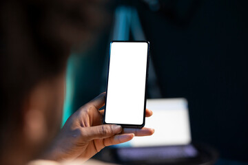 BIPOC man chatting with online friends using mockup phone in warm stylish home, enjoying himself. Person scrolling on isolated screen cellphone, relaxing by scrolling on social media