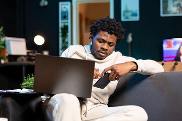 Remote employee at home on couch receiving text from manager, urging him to finish project. Man in...