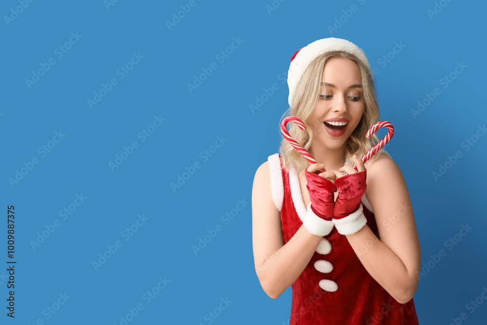 Poster Beautiful young woman dressed as Santa Claus with candy canes on blue background