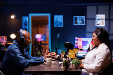 African american male show host interviews smiling woman, conducting a live online discussion . Black couple wearing wireless headphones and recording a podcast for streaming platforms.