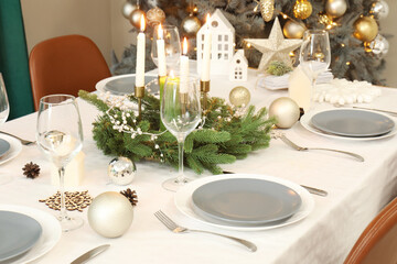 Festive table setting with burning candles, wine glasses and Christmas decorations, closeup