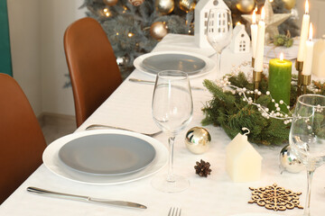 Festive table setting with burning candles, wine glasses and Christmas decorations, closeup