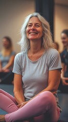 A photo of a middle-aged woman smiling, sitting on the floor in a yoga studio with friends doing poses behind her