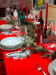 Christmas set table is adorned with festive decorations, ready for a joyful winter holiday gathering. Vibrant red tablecloth and elegant tableware create a warm and inviting atmosphere