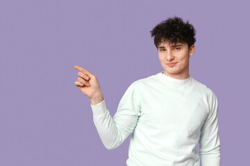 Handsome young man in stylish white sweatshirt pointing at something on purple background