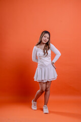 full length beautiful asian woman white top standing smiling elegantly hold back and waist isolated orange background. for technology concept, advertising, broadcast, promotion