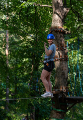 Smiling woman balancing on a tightrope during a rope course adventure in the forest on a sunny day....