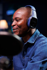Selective focus of african american influencer utilizing professional audio equipment for making podcast episode. Closeup of smiling black man using wireless headset and microphone in his radio show.