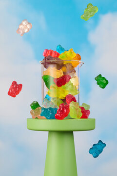 Gummy Bear Candy explosion in Glass Beaker on chartreuse pedestal with blue sky and cloud background Happy and Joyful 