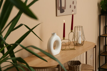 Stylish candles on commode near beige wall at home