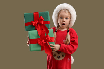 Shocked little girl in Santa hat with Christmas presents on green background