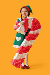 Cute little girl in elf costume with candy cane pinata on yellow background