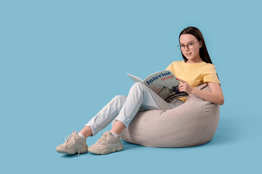 Teenage girl reading magazine on beanbag against blue background