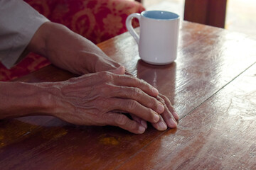 two hand of senior elder on table, loneliness old man in living room with his coffee glass with window view