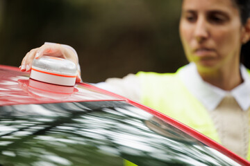 Young woman with reflective vest, places the V16 emergency light beacon on the roof of the damaged vehicle. Help flash, mandatory to replace triangles in Europe. DGT Spain.