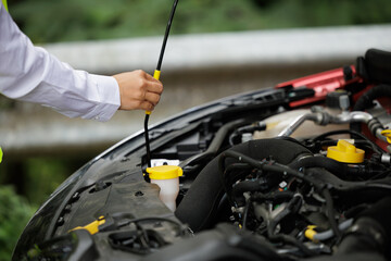 a young woman's car breaks down on her vacation trip and she opens the hood of the car to look at the engine and see if she can fix it or if she should call the insurance to send a tow truck.