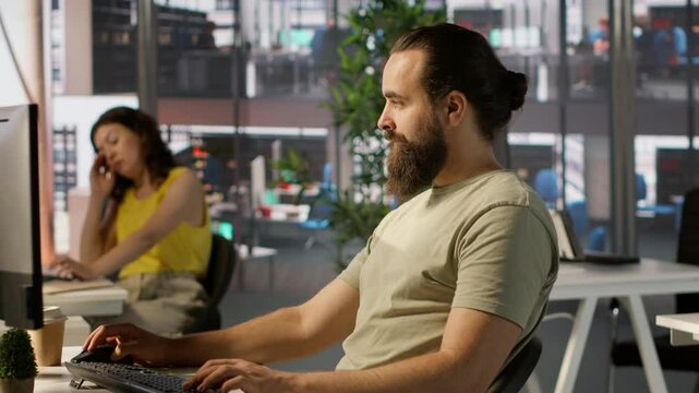 Meticulous staff member imputing data on computer in office. Adept worker at desk focused on typing company statistical numbers, working hard to finish job before deadline, camera A