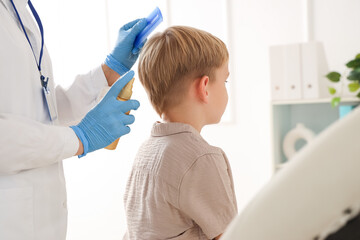 Female doctor with remedy brushing little boy's hair with pediculosis in clinic