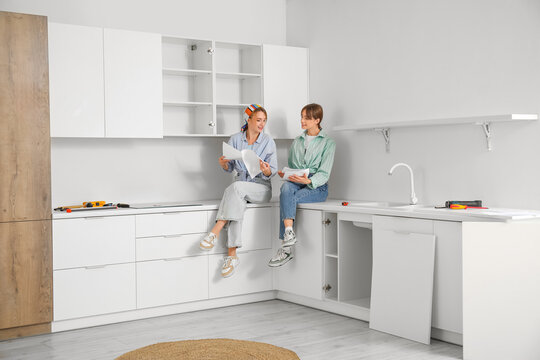Young women with furniture assembling instructions sitting on table in kitchen