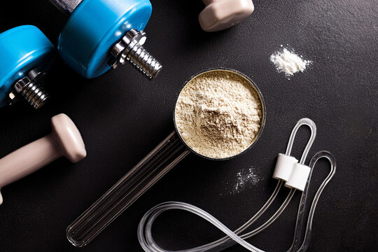 proteina whey con scoop sobre un fondo negro con pesas de entrenamiento, concepto de salud fitness fuerza y suplementos proteicos