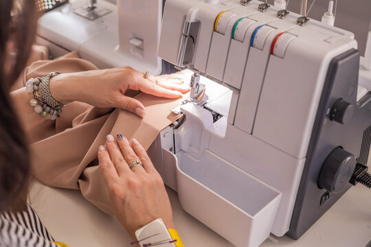 A plus size woman fashion designer uses an overlock sewing machine in her studio. A seamstress sews